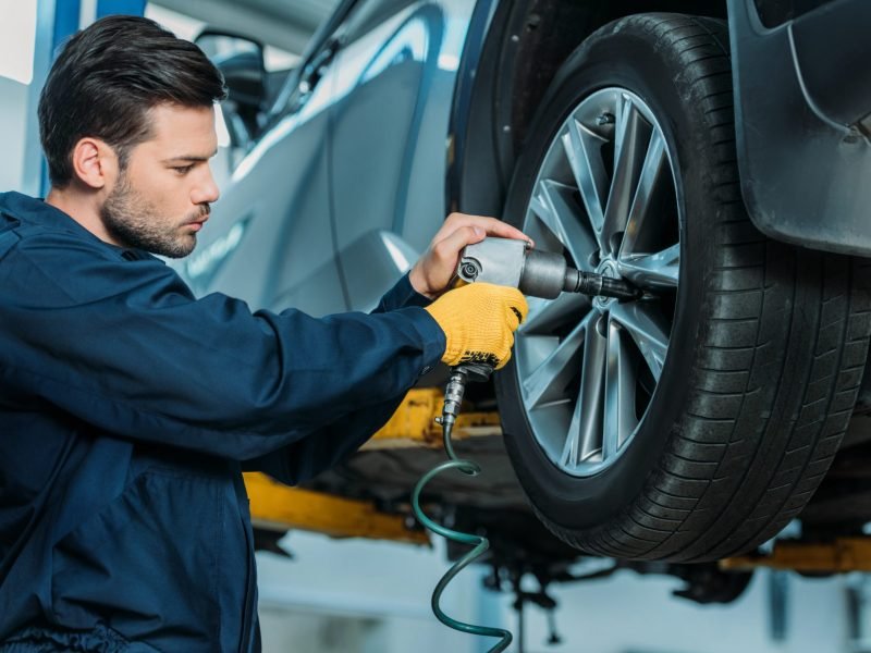 Automechanic unscrewing tire bolts on a lifted up car at a repair shop.