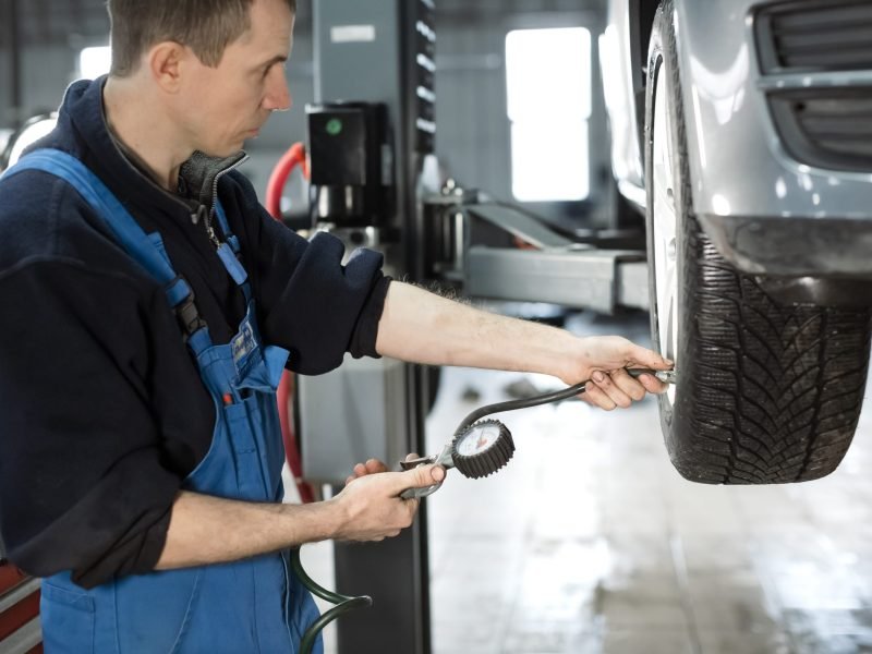 Mechanic checking tire pressure in car wheel at service station